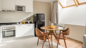 Eine moderne Küche mit weißen Schränken, einer eingebauten Mikrowelle und einem schwarzen Kühlschrank. Ein runder Holztisch mit Obstschale und zwei braunen Stühlen.