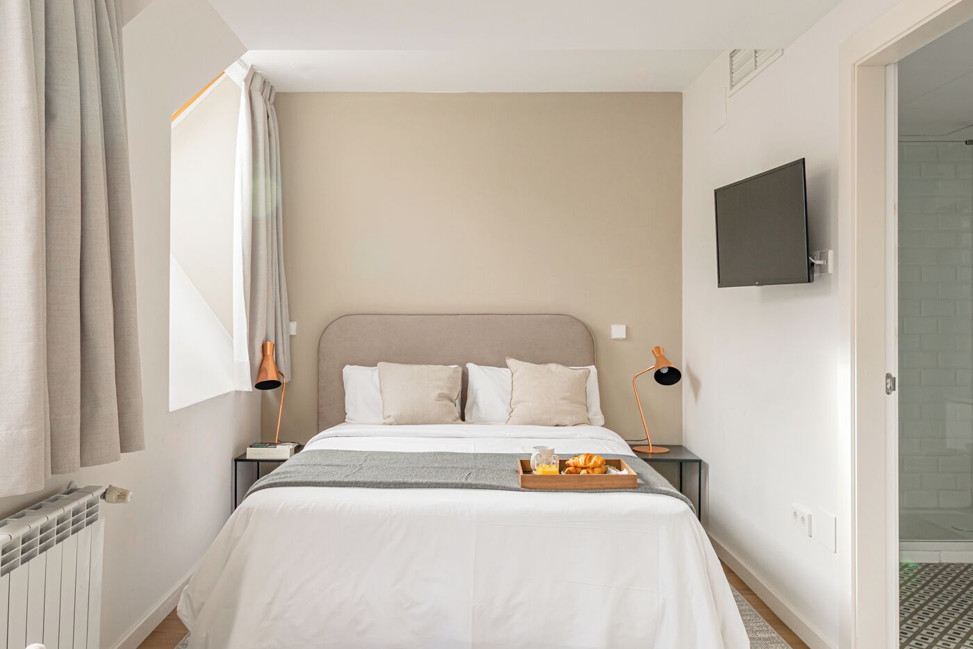 A bedroom with a bed, bedside tables, a TV, and a breakfast tray.