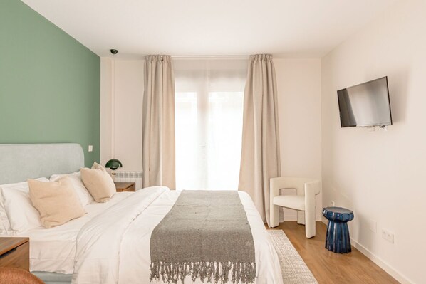 Un dormitorio con una cama, un televisor montado en la pared y una silla.