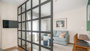 Ein modernes Wohnzimmer mit Schiebeglasfenster, einem Flachbildfernseher, einem grauen Sofa, einem Holzessttisch und einem gerahmten abstrakten Kunstwerk.