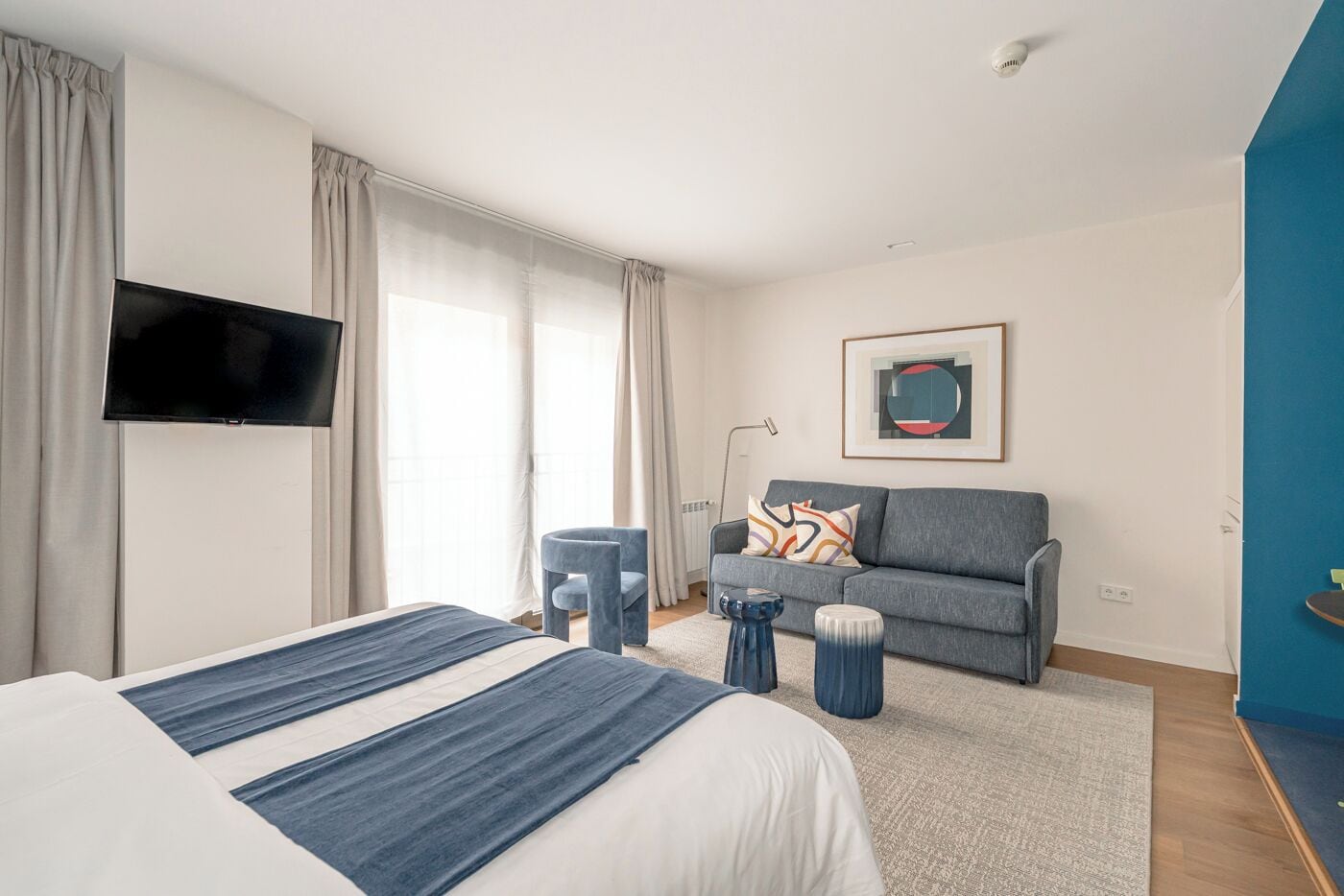 A hotel room with a bed, a sofa, a TV, and a painting on the wall.