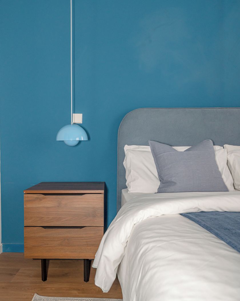 Un dormitorio con cama, mesita de noche y lámpara de pared.