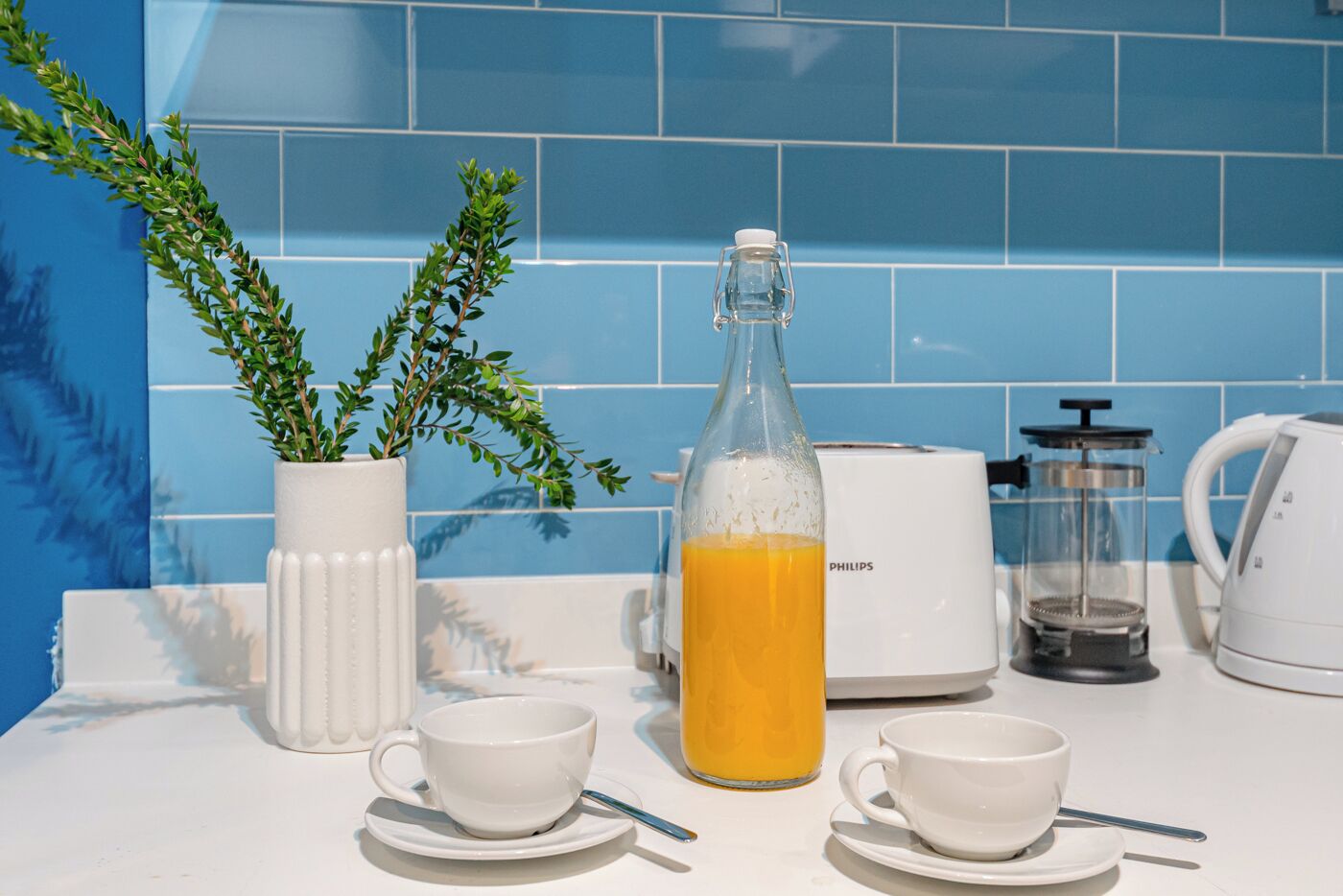 En køkkenbordplade med kaffemaskine, et glas kande, en hvid kop og en potteplante.