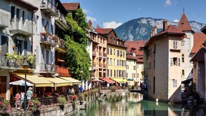 A canal with buildings on either side, a bridge, and mountains in the background.