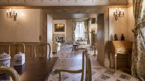 A formal dining room with a wooden table, chairs, and a chandelier. There is a sofa and a lamp in the background.