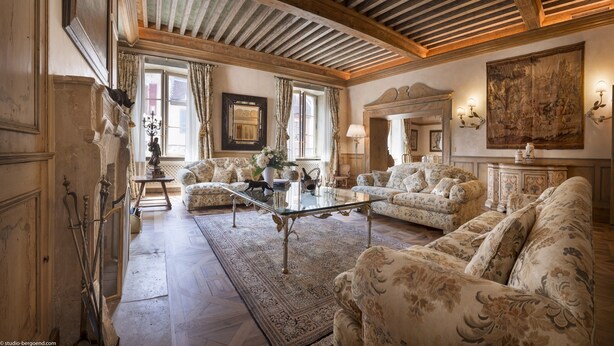 A spacious living room with a high ceiling, ornate furniture, and a large painting on the wall.