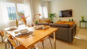 A modern living room with a dining area, a sofa, a TV, and a plant. - Sebastian Patio by Hello Homes Sitges (Sitges)