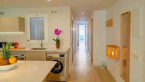 A modern kitchen with a washing machine, a sink, and a window. There is a hallway leading to a bedroom. - Sebastian Patio by Hello Homes Sitges (Sitges)