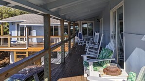 A covered porch with white rocking chairs and a table with a dog bowl. - Ocean View, large deck, private, nearby beach access  (Pine Knoll Shores)