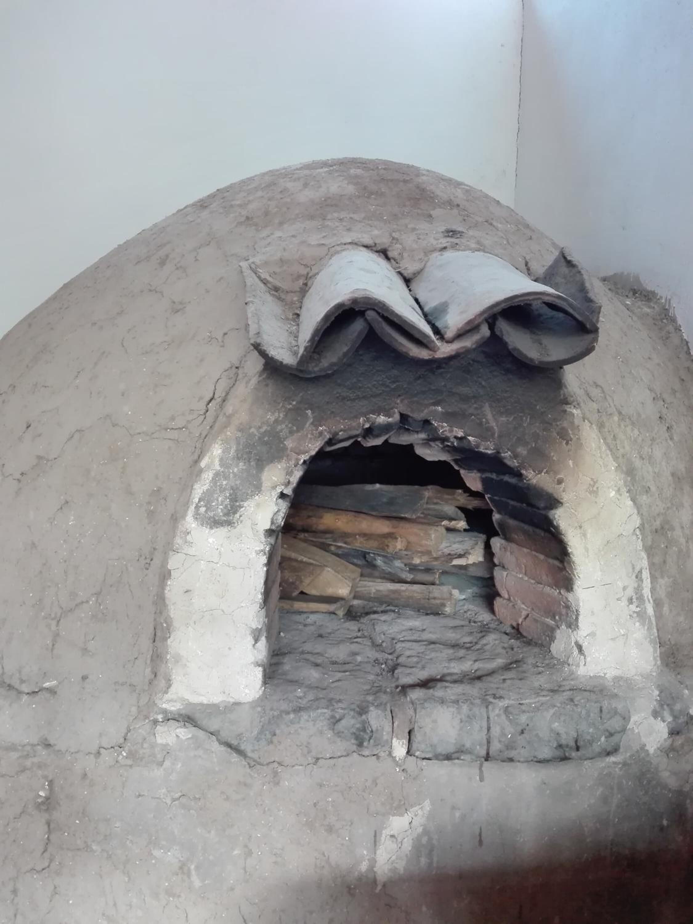 Un horno de ladrillo tradicional con estructura de piedra, leña en su interior y un diseño rústico sencillo.