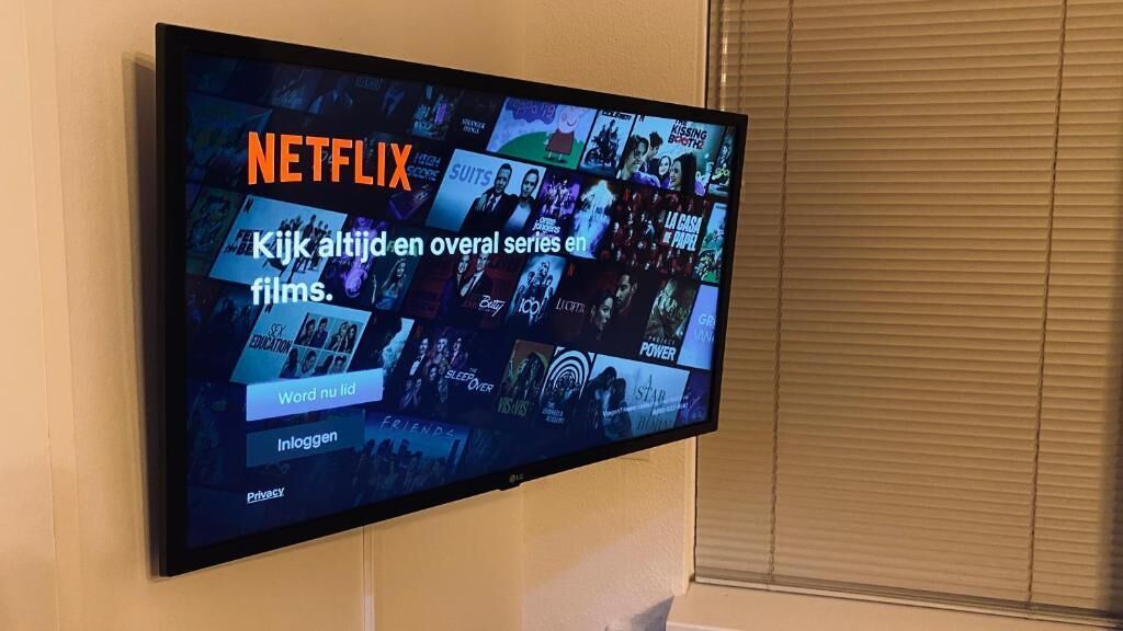 Un téléviseur fixé au mur affiche l’interface de Netflix, avec différentes vignettes de films.