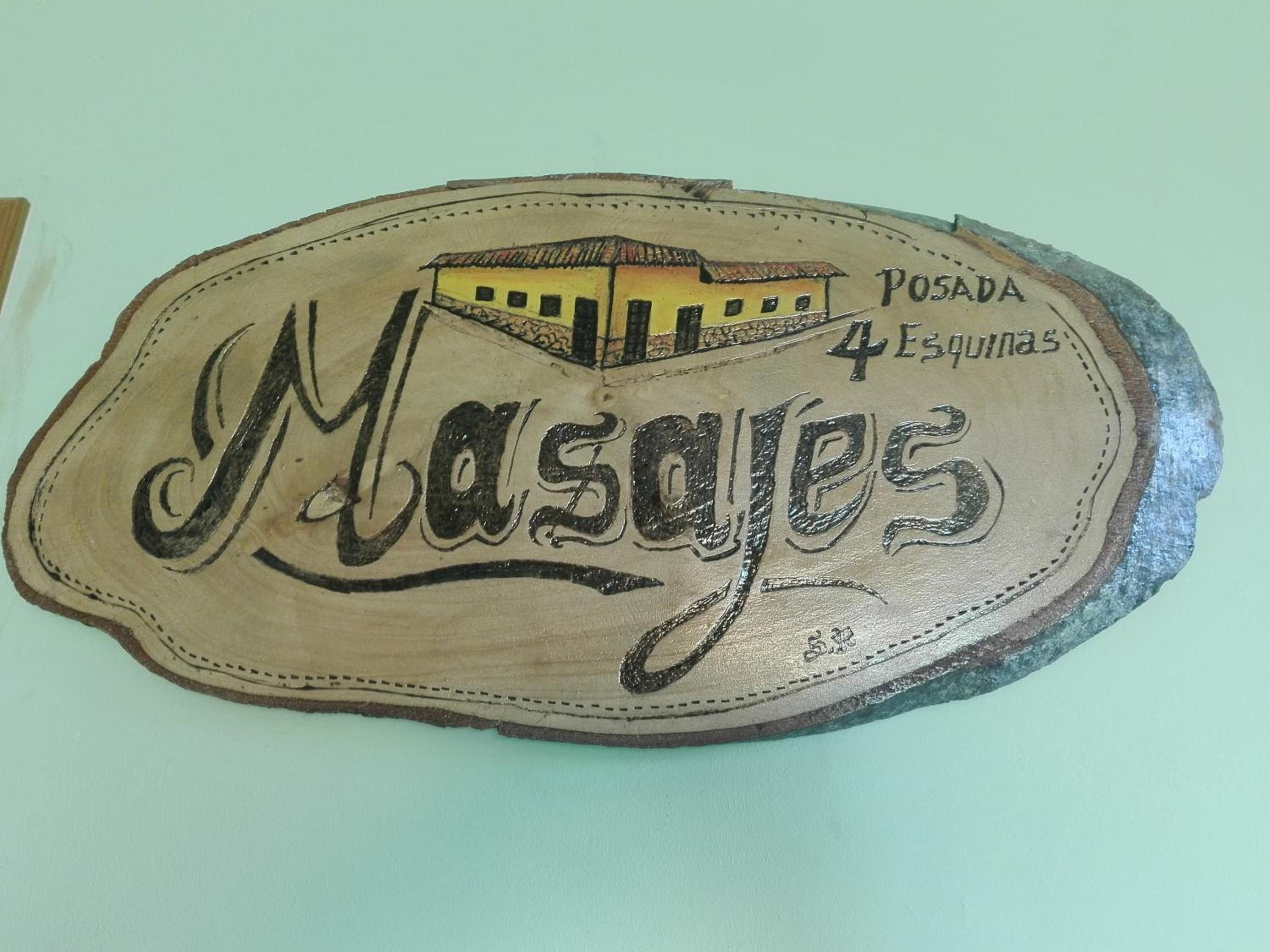 A wooden plaque with the text 'Masajes Posada 4 Esquinas' and a building illustration.