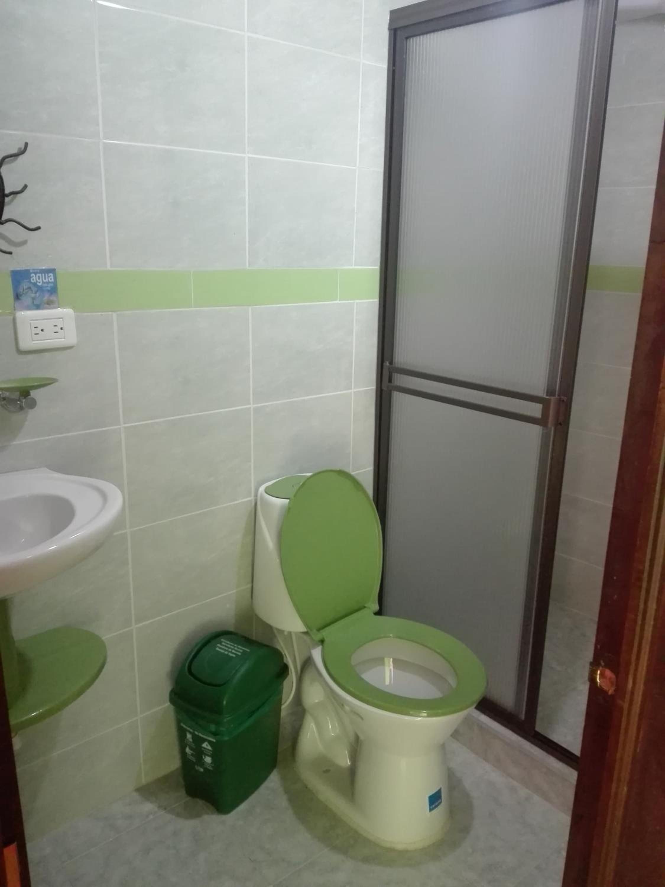 Ein kleines Badezimmer mit Toilette, Waschbecken und einer grünen Mülltonne.
