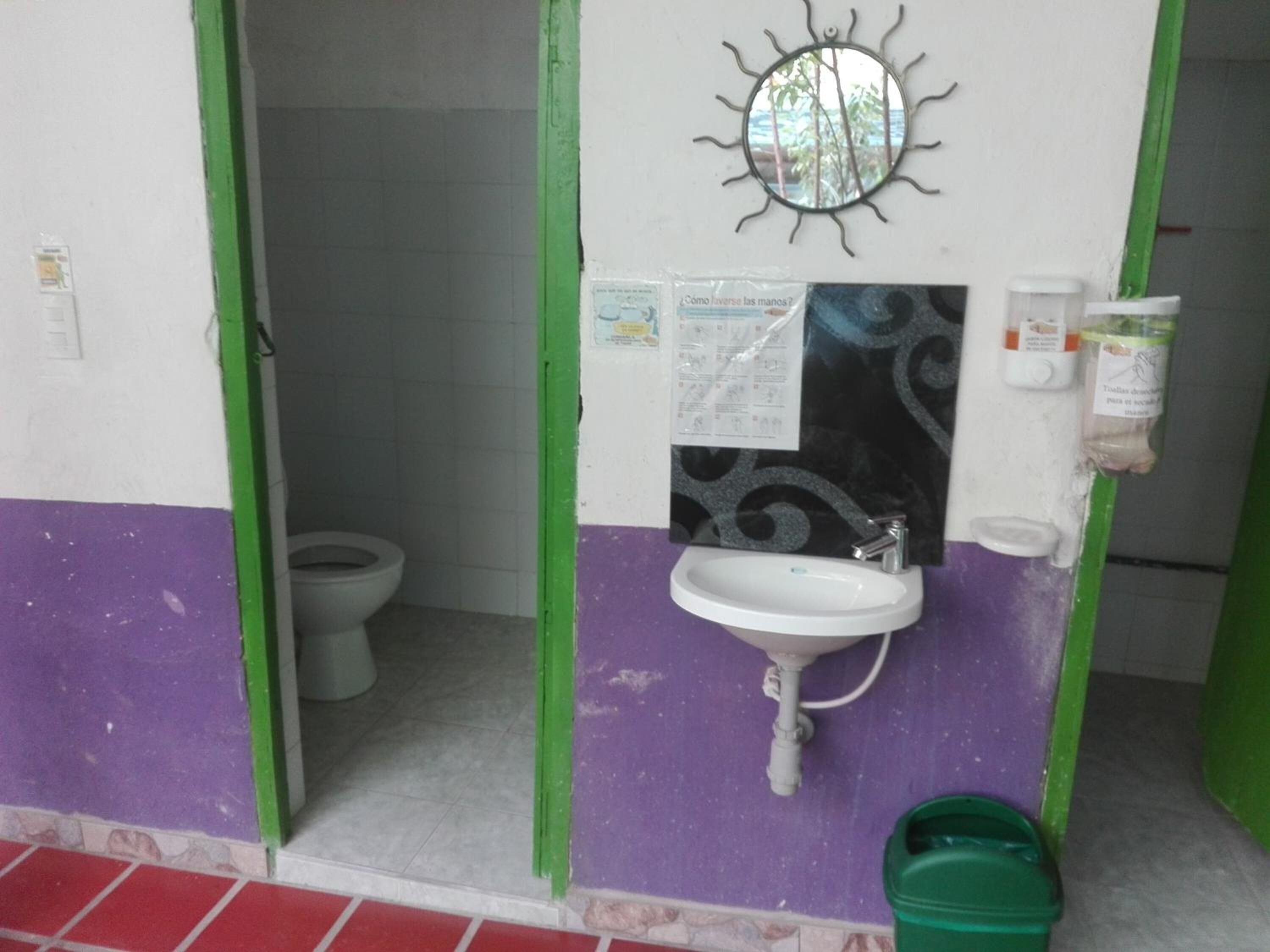 Une petite salle de bain avec un lavabo blanc, un miroir et un seau vert.