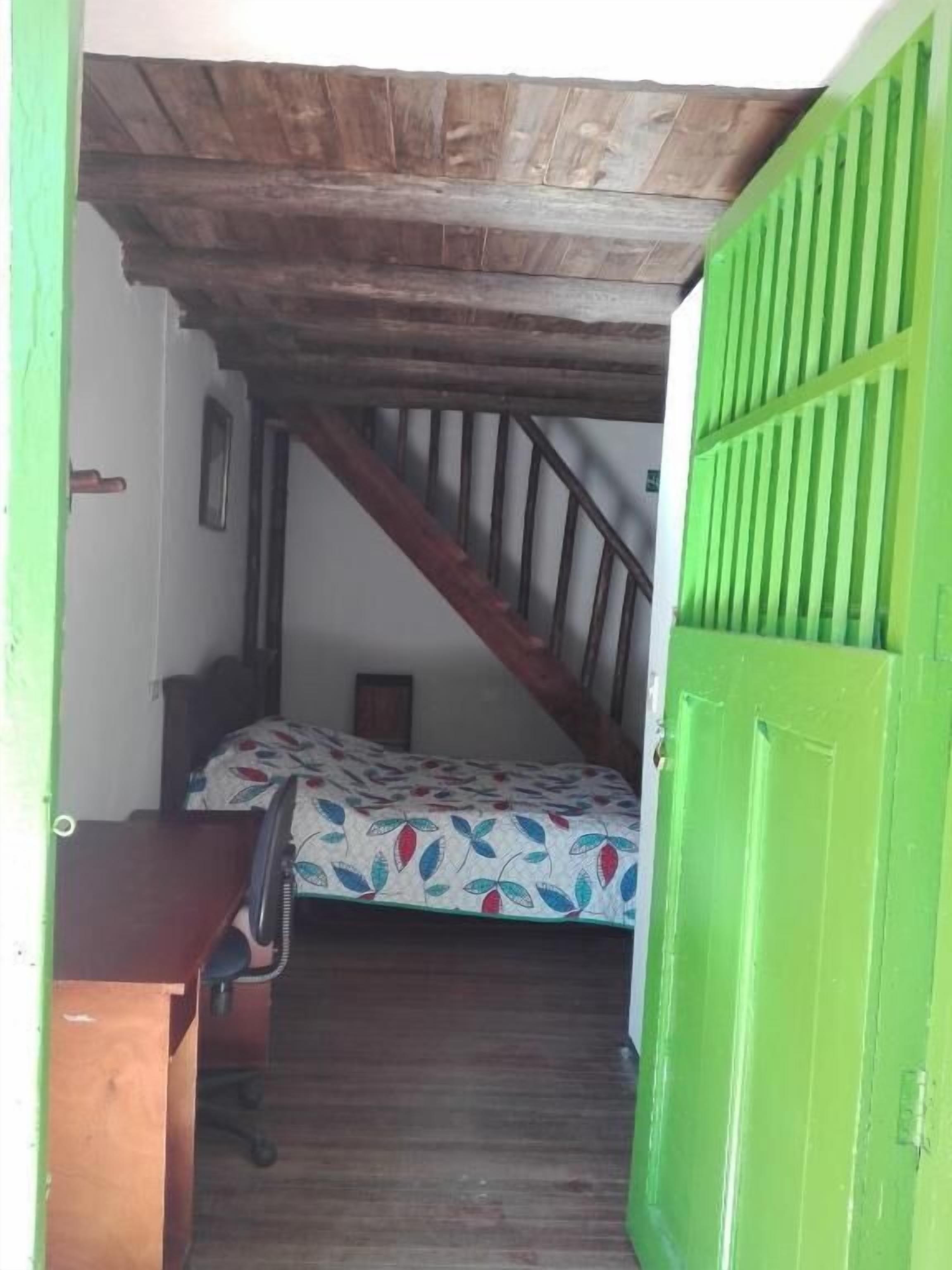 A room with a bed, a desk, a chair, and a green door.