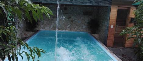 A rectangular hot tub with a stone wall and a wooden balcony railing.