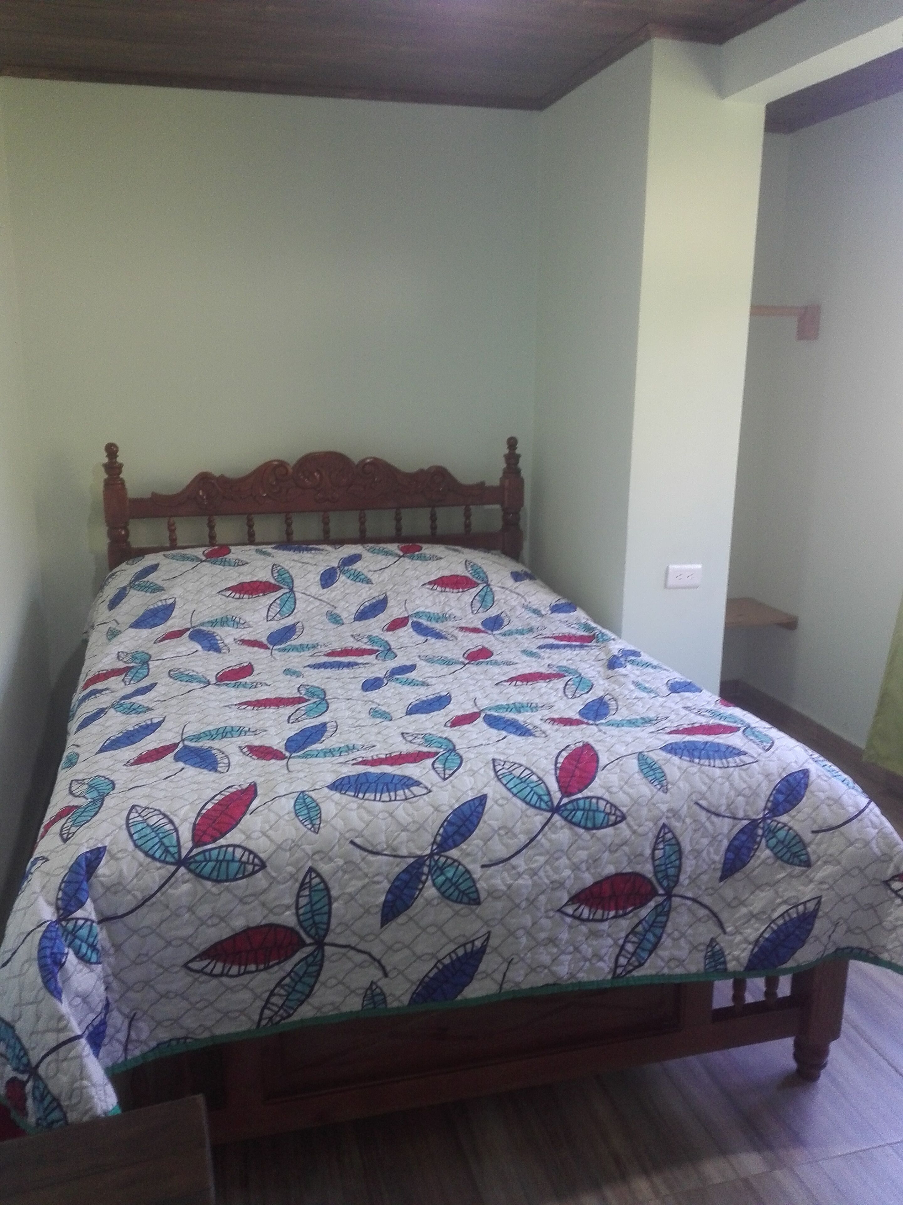 A single bed with a floral-patterned bedspread in a room with a wooden headboard and a plain wall.