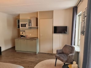 A compact living space with a kitchenette, a flat-screen TV mounted on the wall, and a seating area with a chair. - Posada 4 Esquinas (La Uvita)
