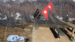 Eine Person steht auf einer Betonplatte, hält eine Flagge, raucht eine Wasserpfeife und ein blau kariertes Tuch liegt auf dem Boden.