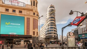 Une place animée en plein centre-ville, avec un grand panneau publicitaire Movistar bien visible, un panneau indiquant l’entrée du métro et le cinéma Cines Callao.