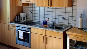 A kitchen with wooden cabinets, a stainless steel oven, a coffee maker, and a microwave. - Apartment in the beautiful biosphere reserve on Rügen (Lancken-Granitz, Rügen)