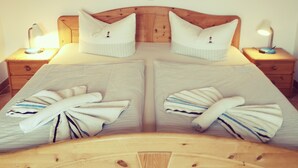 Una cama doble con cabecera de madera, dos mesitas de noche con lámparas, y un cuadro de un atardecer sobre el océano en la pared.