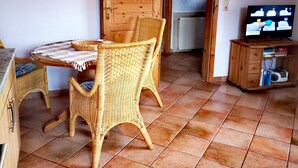 Una habitación acogedora con puerta de madera, una silla de mimbre, una mesita y un televisor sobre un mueble de madera.