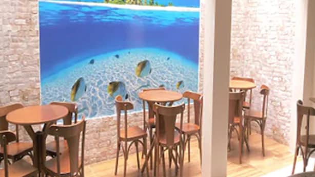 A restaurant with a large mural of a tropical beach scene, wooden tables and chairs, and a stone wall. - Hotel Puçá (Balneário Camboriú)