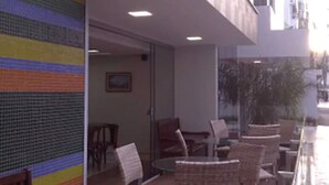 An outdoor seating area with wicker chairs and tables, a colorful wall, and a view of the street. - Hotel Puçá (Balneário Camboriú)