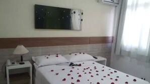 A hotel room with a bed, a nightstand, a lamp, an air conditioner, and a painting on the wall. - Hotel Puçá (Balneário Camboriú)
