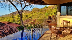A balcony with a glass barrier, outdoor seating, and a view of a mountainous landscape. - Casa 36 Hermosa Heights (Sardinal)