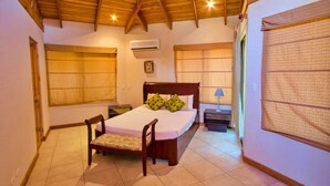 A bedroom with a wooden ceiling, a bed with pillows, a chair, a nightstand, and a window with blinds. - Casa 36 Hermosa Heights (Sardinal)