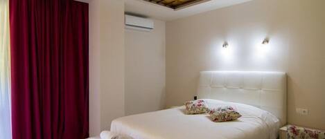 A hotel room with a wooden ceiling, a large bed with white bedding, two wall-mounted lights, and a red curtain.