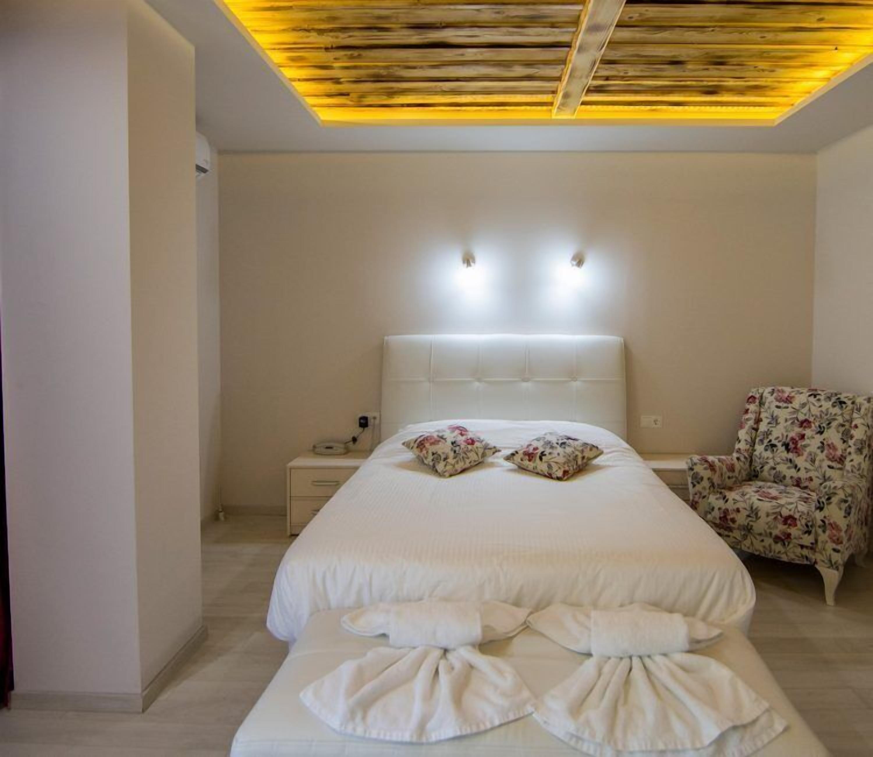 A bedroom with a large bed, a nightstand, a chair, and a ceiling with wooden slats and recessed lighting.