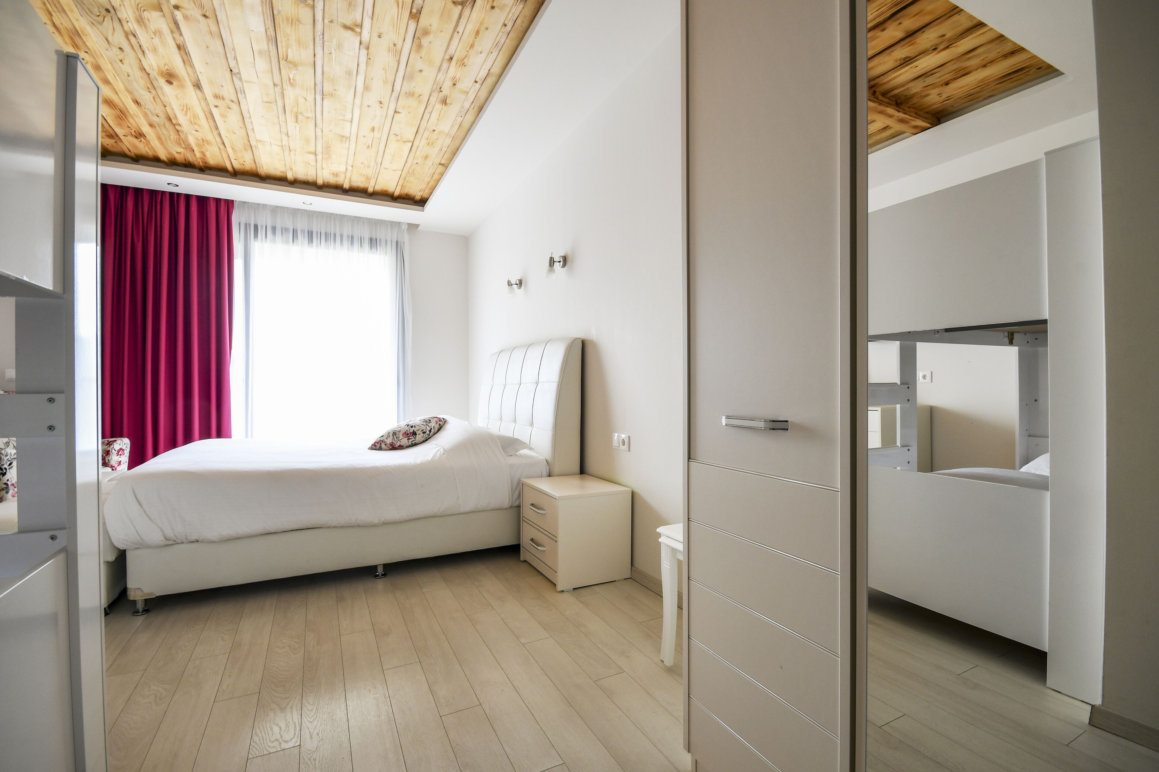 A modern bedroom with a wooden ceiling, a bed with white bedding, a nightstand, and a built-in wardrobe.