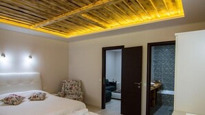 A modern bedroom with a large bed, a wooden ceiling, and a view into a bathroom. - Archontiko Liamas (Volvi)