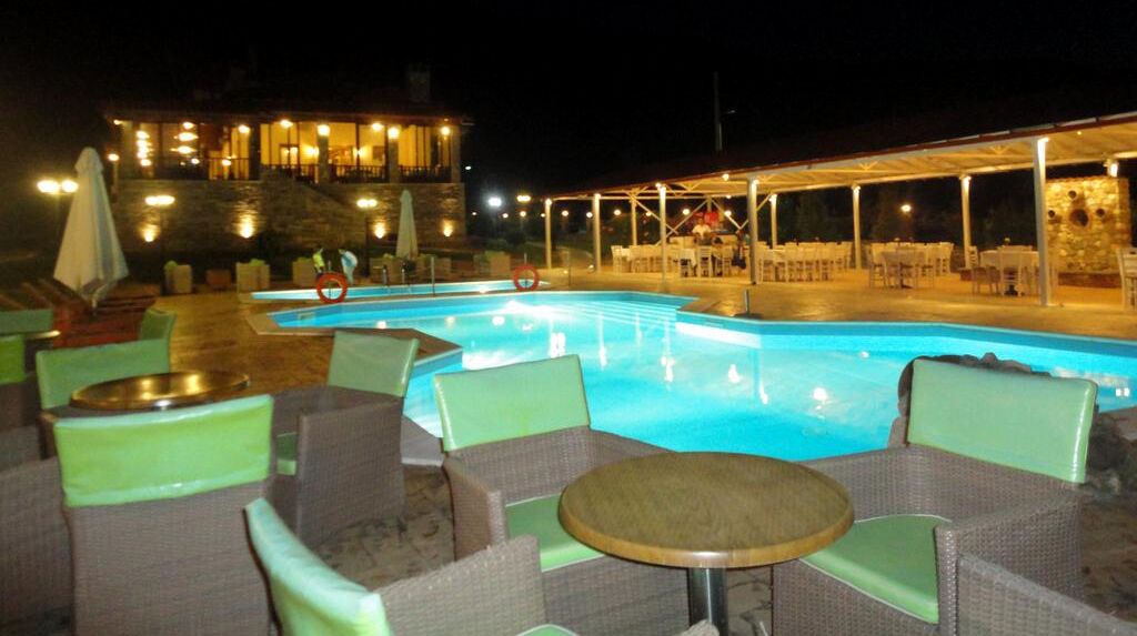 Un espace extérieur avec une piscine, des chaises longues et des tables, un coin salon abrité et un bâtiment en arrière-plan.