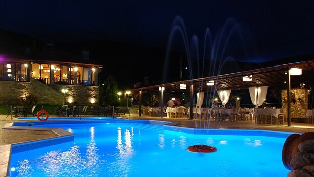 A nighttime swimming pool with water fountains, outdoor seating, and a building with illuminated windows. - Archontiko Liamas (Volvi)