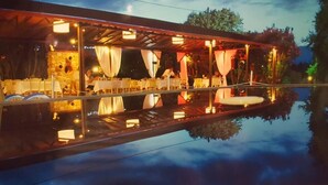 An outdoor restaurant with tables and chairs under a covered area, reflecting on a calm body of water. - Archontiko Liamas (Volvi)