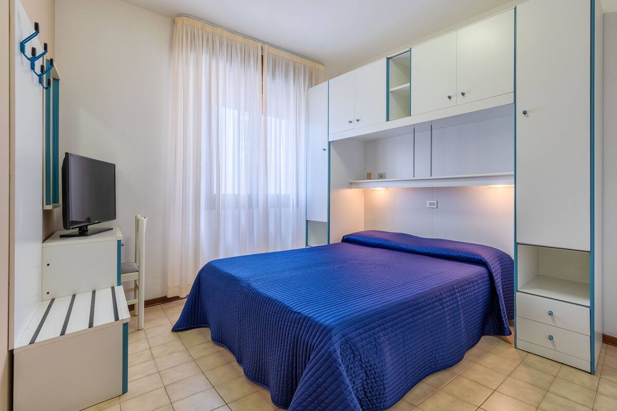A bedroom with a bed, a TV, a desk, and a wardrobe.