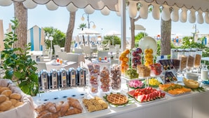 A buffet with various food items and beverages, set in an outdoor area with tables and chairs, overlooking a beach. - Hotel Sanremo (Jesolo)