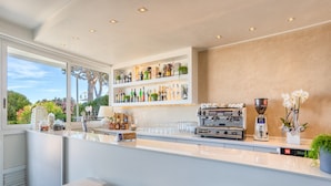 A modern bar area with shelves of bottles, a coffee machine, and seating. - Hotel Sanremo (Jesolo)