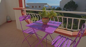 A balcony with a purple table and matching chairs, a potted plant, and a view of the sea and buildings. - La Zagara (Furci Siculo)