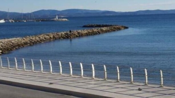 Un paseo marítimo con un muro de piedra y una barandilla de metal.