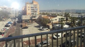 Vista de un puerto deportivo con barcos, un estacionamiento y edificios al fondo.