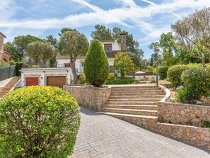 A stone staircase leading to a building with a red garage door, surrounded by well-maintained greenery and a clear sky.