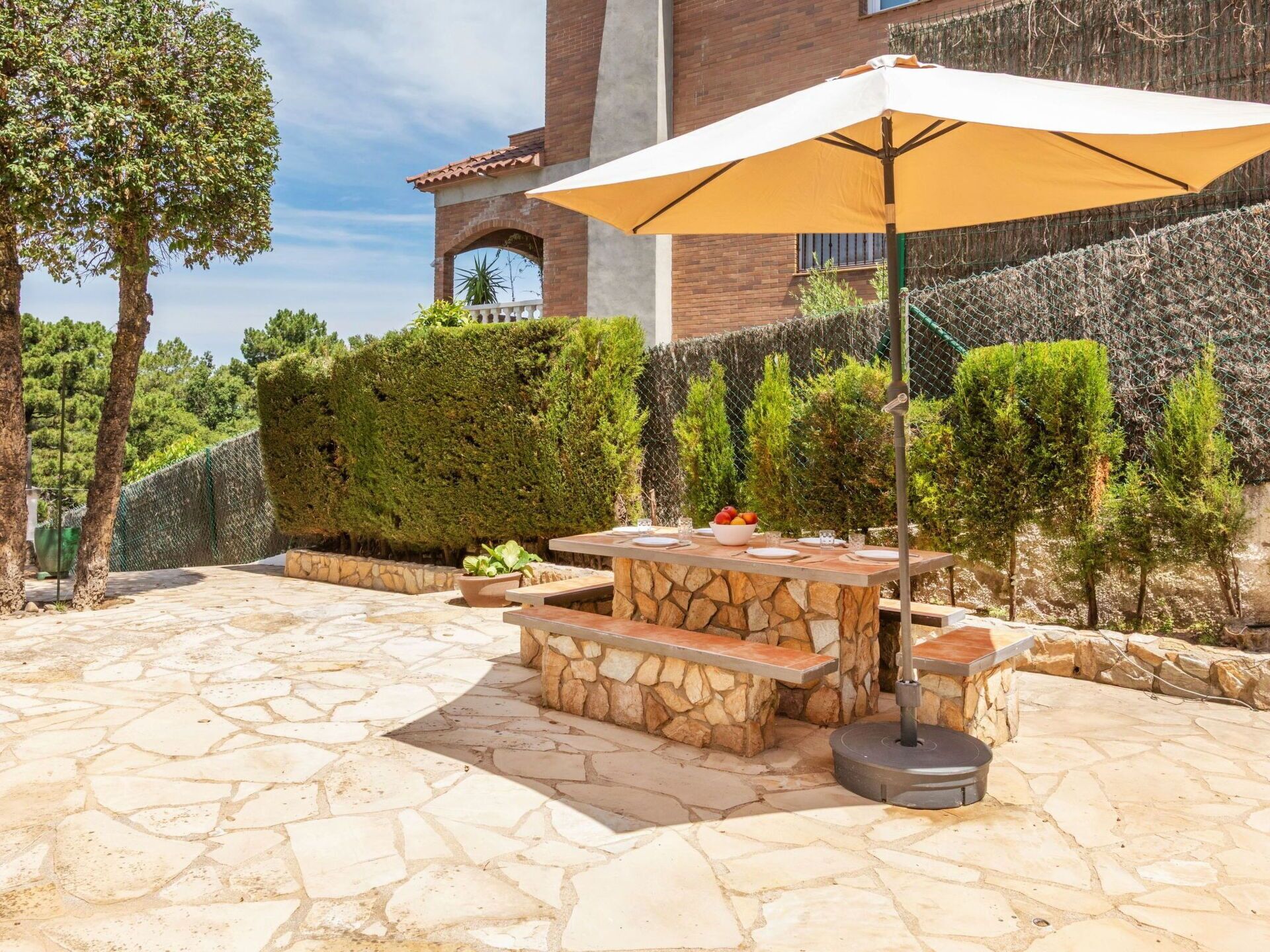 Une terrasse extérieure avec une table et un banc en pierre, entourée d’un sol en pierre et d’une clôture.