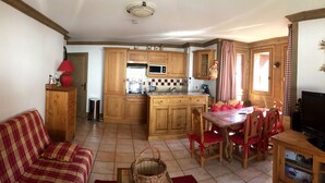 A cozy living room with a sofa, a dining table with chairs, a television, and a kitchen area with wooden cabinets and a microwave. - B205 - 58 m2 - 3P - 6 pers (Prapoutel)