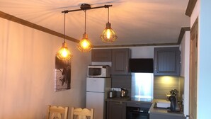 A compact kitchen with a dining area, featuring a wooden table and chairs, a microwave, a kettle, and a stove. - F101 - 40 m2 - 2P - 2/4 pers (Prapoutel)