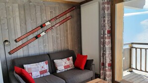 A room with a grey sofa, two red pillows, a wooden coffee table, and a wooden wall with two red and white striped objects. - F101 - 40 m2 - 2P - 2/4 pers (Prapoutel)